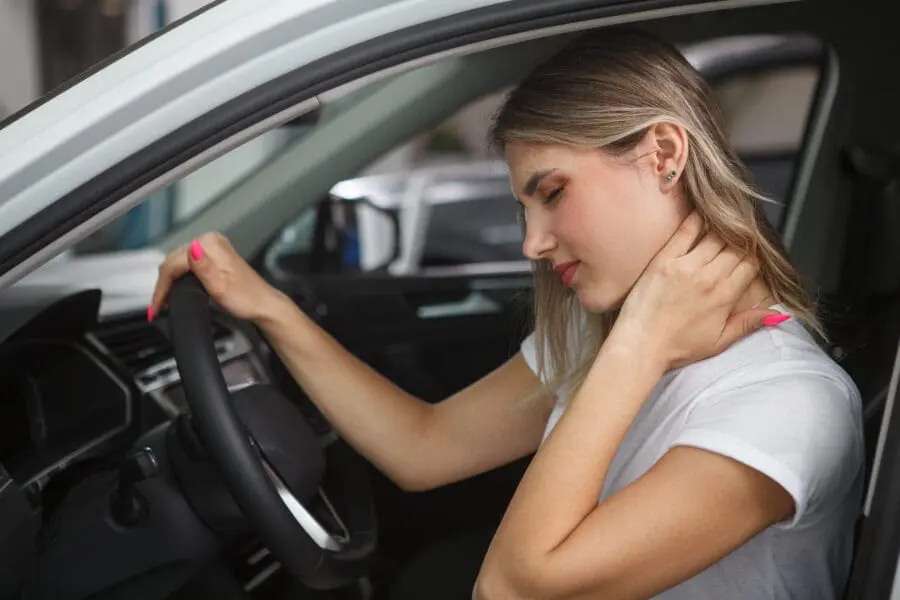 a woman holding her neck and looking at the wheel of a car. Common Injuries from Car Accidents
