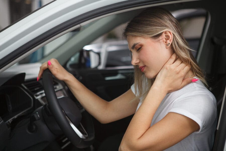 a woman holding her neck and looking at the wheel of a car. Common Injuries from Car Accidents