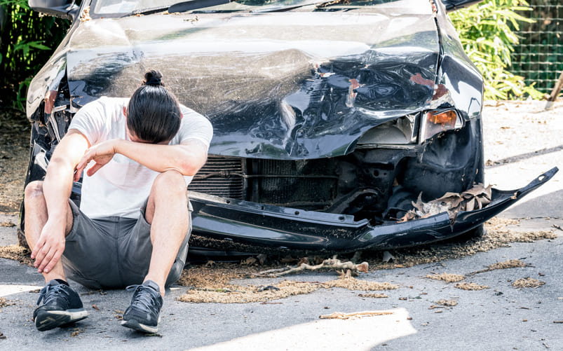 driver sitting in front of totaled leased car after accident