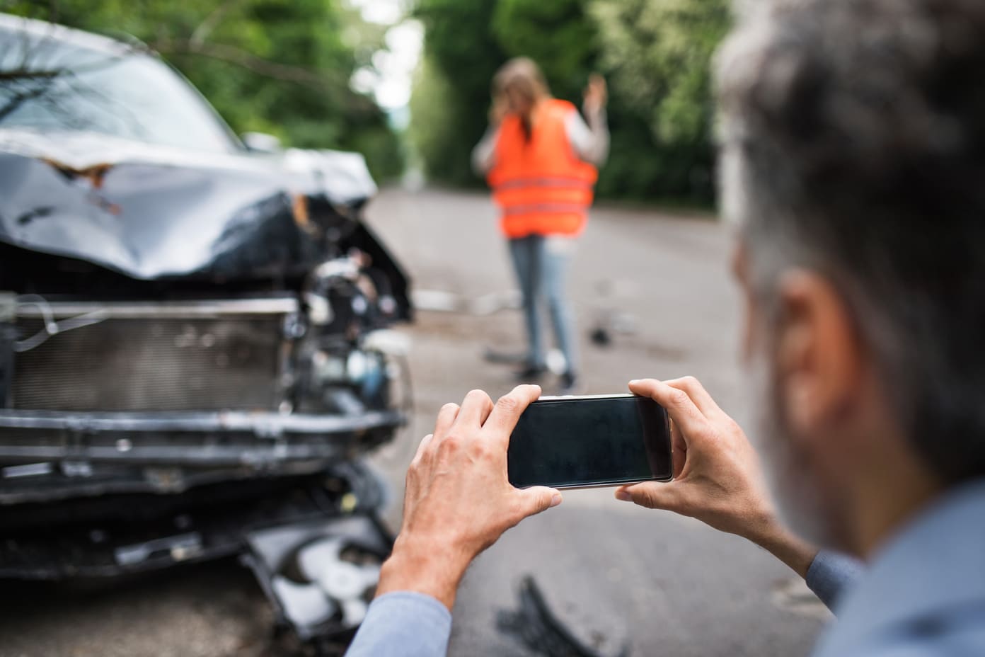 man taking pictures of damage after car accident with uninsured driver