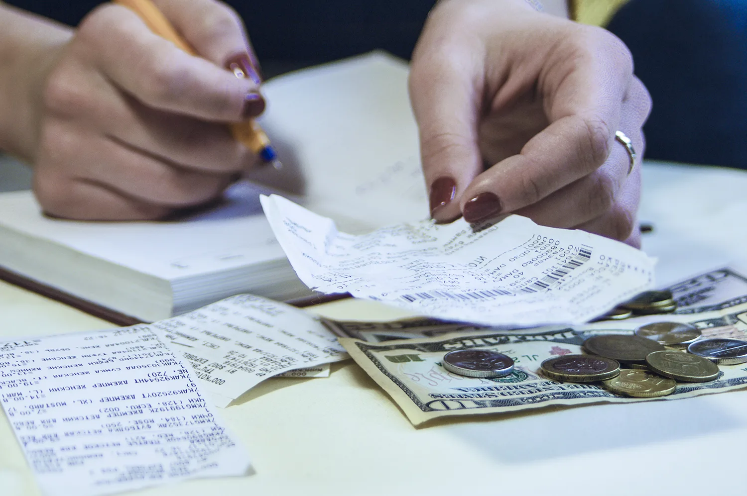Los recibos en la mesa se superponen al dinero mientras alguien anota los totales en un bloc de notas